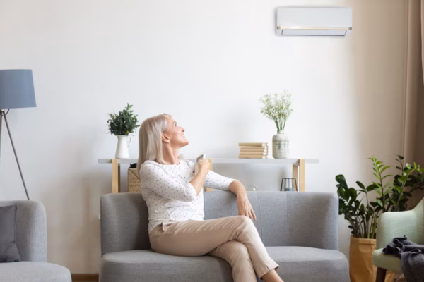 Femme réglant la télécommande de sa climatisation, assise dans un salon