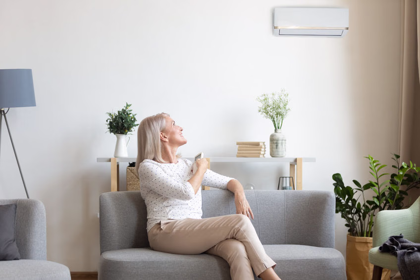Femme réglant la télécommande de sa climatisation, assise dans un salon
